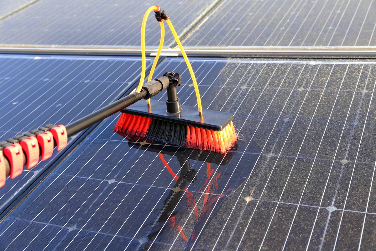 A brush on an extension pole being used to wash a solar panel.