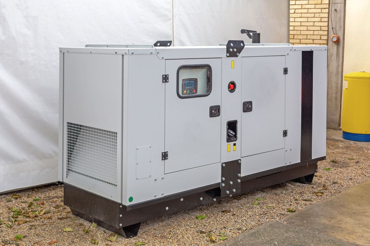 A white enclosed standby generator installed on gravel beside a building.