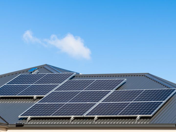 Solar panels tilt-mounted in a row along a dark metal roof.